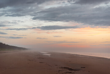 Empty sandy beach of Baltic sea covered with fog after rain during the sunset at summer