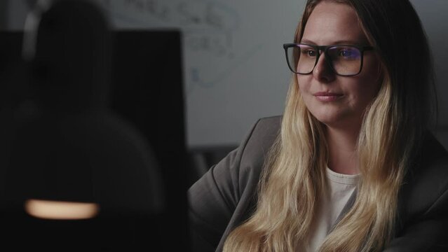A young charming blonde businesswoman in glasses sits at workplace at the table, uses a computer, reads, says wow and demonstrates thunderstruck pleasant surprise on face. The concept of openness in