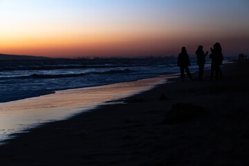 Fototapeta premium Shoreline of Huntington City Beach at Sunset, with Silhouettes of Multiple People, California, USA, horizontal
