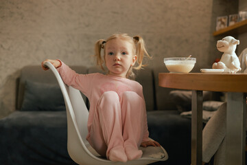 baby kids little girl sitting on the table and playing with glassware, stylish clothes, ponytail...