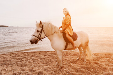 A woman in a dress stands next to a white horse on a beach, with the blue sky and sea in the...