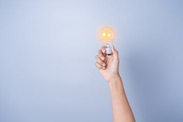 Young woman's hand holding a light bulb, glowing yellow light, electric energy Innovation in science and technology, brainstorming ideas, creating new inspiration a gray studio background.