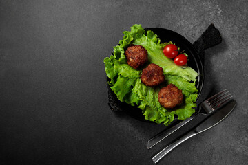 Fried cutlets on a lettuce leaf with tomato on a black background