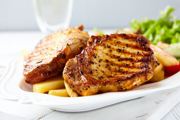 Grilled Steaks with french fries and fresh salad. Bright wooden background.