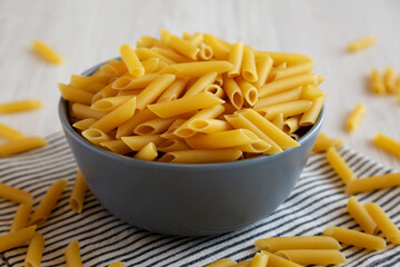 Raw Organic Dry Penne Pasta in a Bowl, side view.