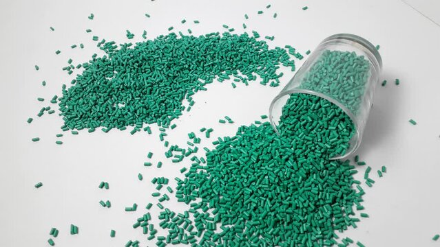 Turquoise masterbatch granules spilling from a sloki on a white background.Color pigment carrier polymers in the plastics industry