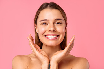 A woman with tattoos smiles against a pink background, radiating cheerful and confident energy