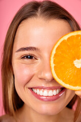 A joyous woman posing with an orange slice, representing skincare and natural beauty ideals