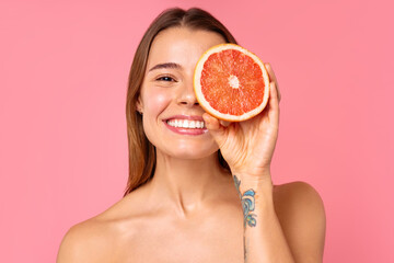 Woman with grapefruit on pink background representing wellness, beauty, and healthy lifestyle