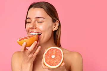 Smiling woman with grapefruit on pink background, symbolizing wellness and healthy eating