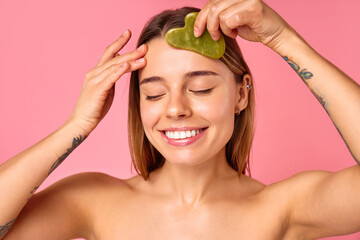 Closeup of a woman using a jade facial roller for skincare and selfcare on a pink background