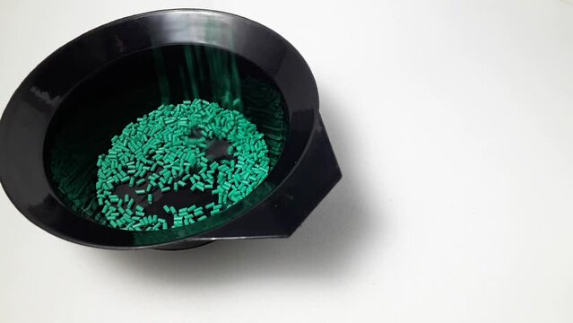 Turquoise masterbatch granules fall into a black measuring cup.Color pigment carrier polymer in the plastics industry