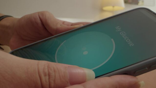 Close up of hands of unrecognizable person checking glucose level using health app on smartphone