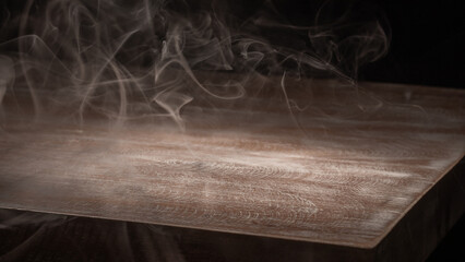 A close-up image of white smoke rising up from a dark brown wooden surface. Background