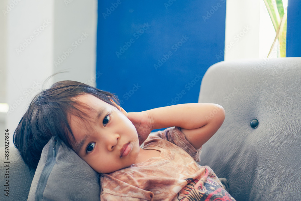 Wall mural little asian boy sitting on a couch and upset with a bored face - Wall murals