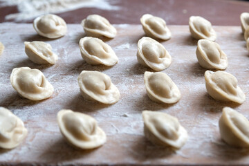 The raw dumplings were placed on a wooden cooking board, sprinkled with flour. The filling is minced meat, potatoes, cheese or cottage cheese. A semi-finished product, ready for cooking.
