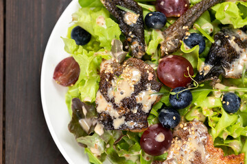 Salad with grilled chicken, grapes, blueberries, and lettuce on a white plate.