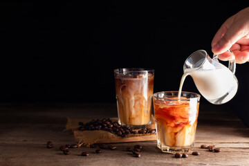 Soft iced coffee with milk, cream, white foam and ice. Coffee latte, espresso, cappuccino, cocktail ready to drink on dark and black background.