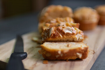 Baked peanut butter cake with nuts on a wooden cutting board with a knife on the side. The bread is topped with sliced nuts.