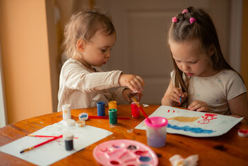 two sisters paint with paints, one is 1 year old and the older one is 5 years old.