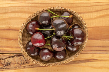 Several ripe sweet cherries with straw plate on wooden table, macro, top view.