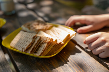 Fresh waffles in a yellow plate under sunlight on wooden table under trees, family picnic, childrens hands near