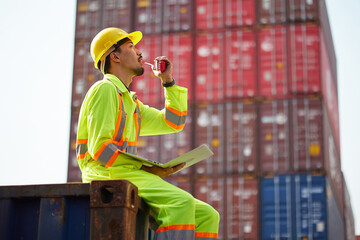 worker or engineer talking on walkie talkie and holding laptop computer in containers warehouse...