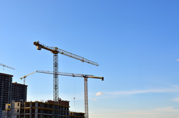 Tower cranes working at construction site on blue sky background. Construction process of the new modern residential buildings