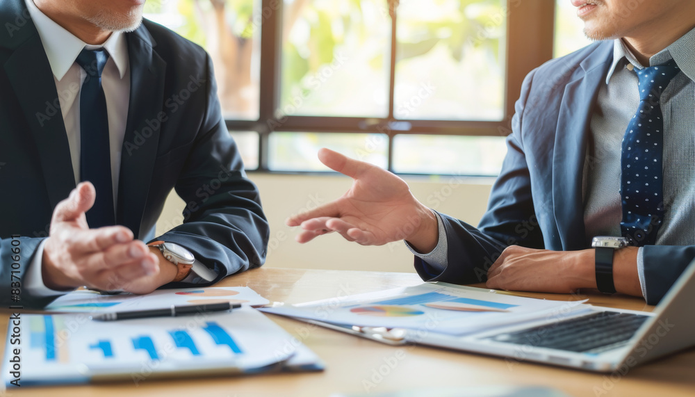 Poster two men in suits are discussing something at a table