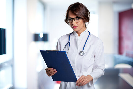 Mid aged felame doctor standing in clinic and holding patient chart in her hand