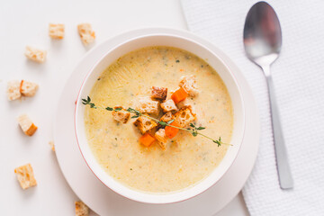 Cream soup garnished with vegetables and croutons with a sprig of thyme on a white table, top view.