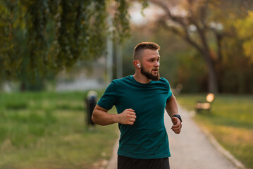 Fototapeta premium Young athletic man running or jogging at the park listening to music on wireless headphones active healthy lifestyle.