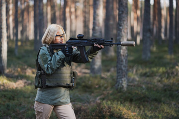 A military girl takes aim from a modern assault rifle in the forest.