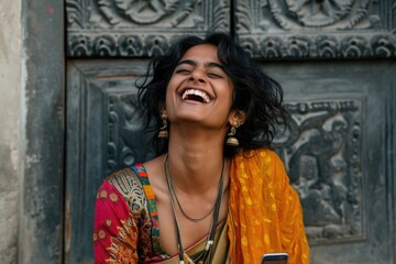 A woman in a colorful sari is smiling and holding a cell phone. Scene is happy and joyful