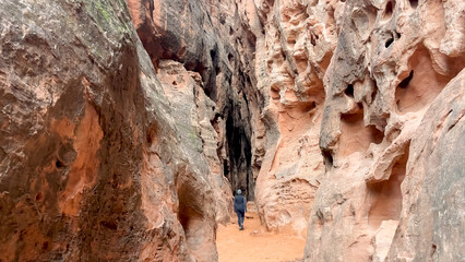 A female hiker walking in Jenny's Slot Canyon surrounded by steep red Navajo sandstone rock walls - Snow Canyon State Park, St George, Utah, USA