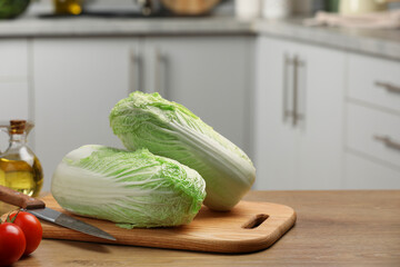 Fresh Chinese cabbages, knife, tomatoes and oil on wooden table in kitchen, space for text