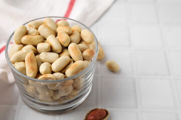 Roasted peanuts in bowl on white tiled table, closeup. Space for text