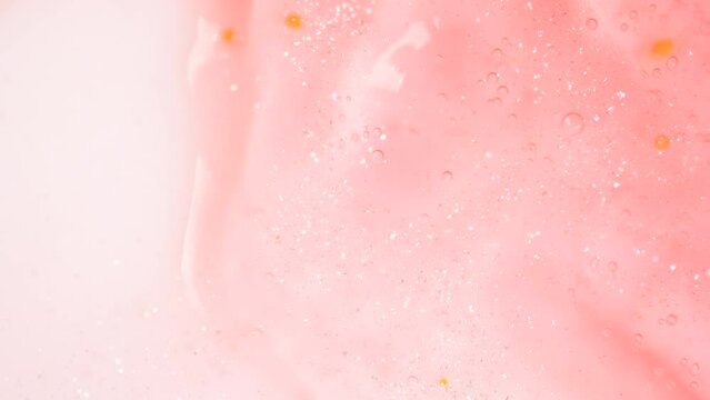 Shimmering shower ger for body flowing on the white surface. Extreme macro of bubbles and glitter in shiny pink shower gel.