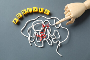 Word Amnesia, brain made of wires and mannequin hand on grey background, flat lay