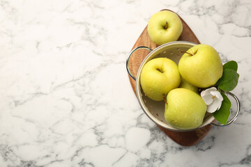 Colander with fresh apples and beautiful spring blossom on white marble table, top view. Space for text