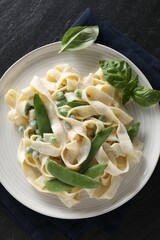 Delicious pasta with green peas and creamy sauce on black table, top view