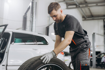 Happy Car Mechanic holding a tire at the repair garage. Replacement of winter and summer tires