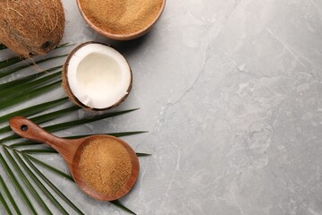 Spoon with coconut sugar, palm leaves, bowl and fruit on grey marble table, flat lay. Space for text