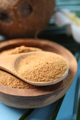 Coconut sugar in bowl, spoon and fruits on light blue wooden table, closeup