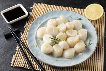 Raw scallops with lemon, rosemary and soy sauce on dark textured table, closeup