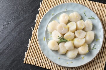 Raw scallops with lemon and rosemary on dark textured table, top view
