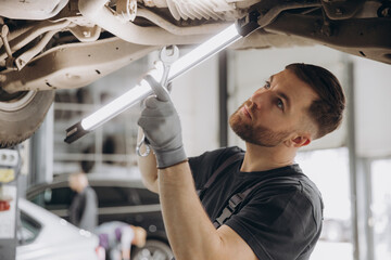 View from side of concentrated worker of car service checking running gear of automobile. Male...