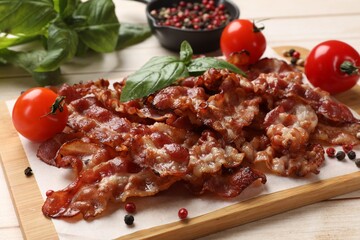 Slices of tasty fried bacon with different spices and tomatoes on wooden table, closeup