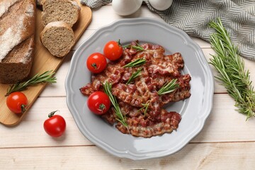 Slices of tasty fried bacon with rosemary and tomatoes served on wooden table, flat lay
