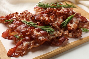 Slices of tasty fried bacon with rosemary on white table, closeup